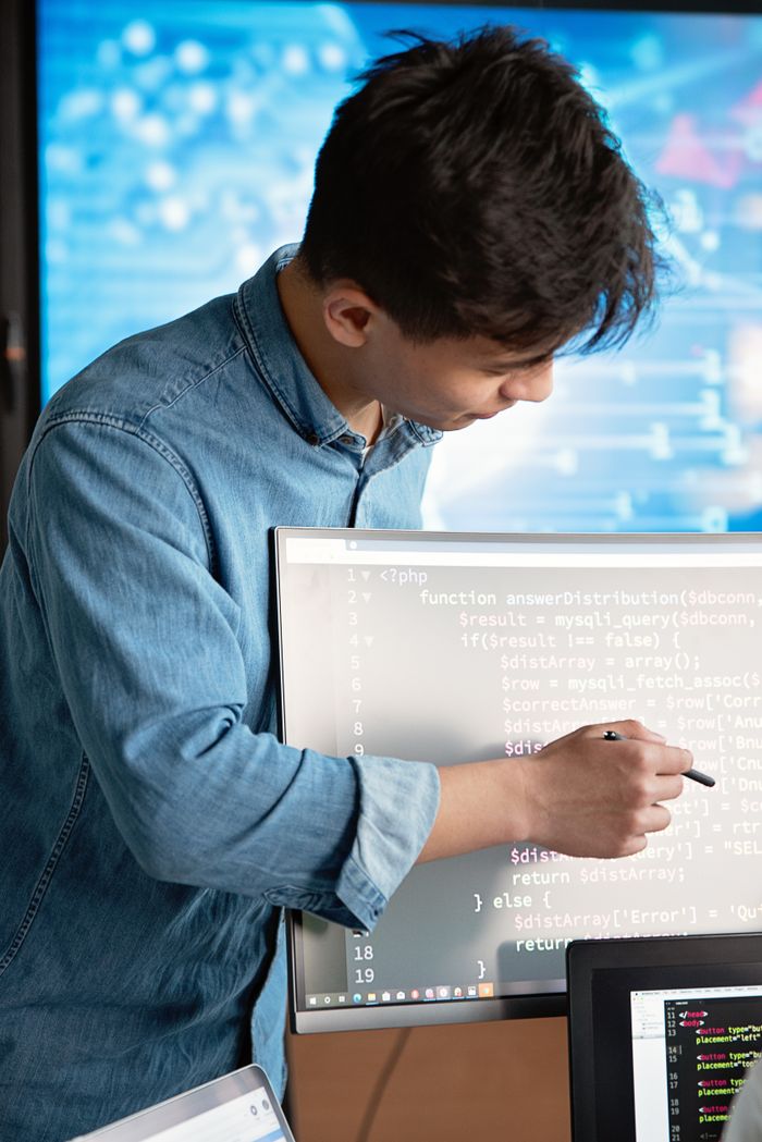 about-img-01 Asian male programmer writing code on a computer monitor in an office setting.